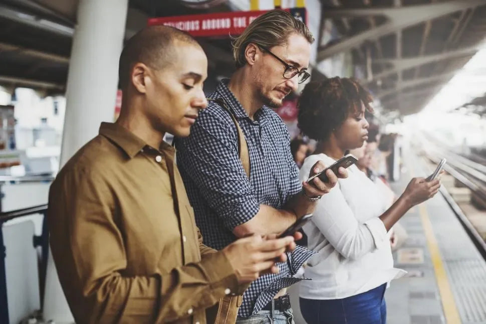 Diverse group of people standing at a train station platform, all focused on their smartphones